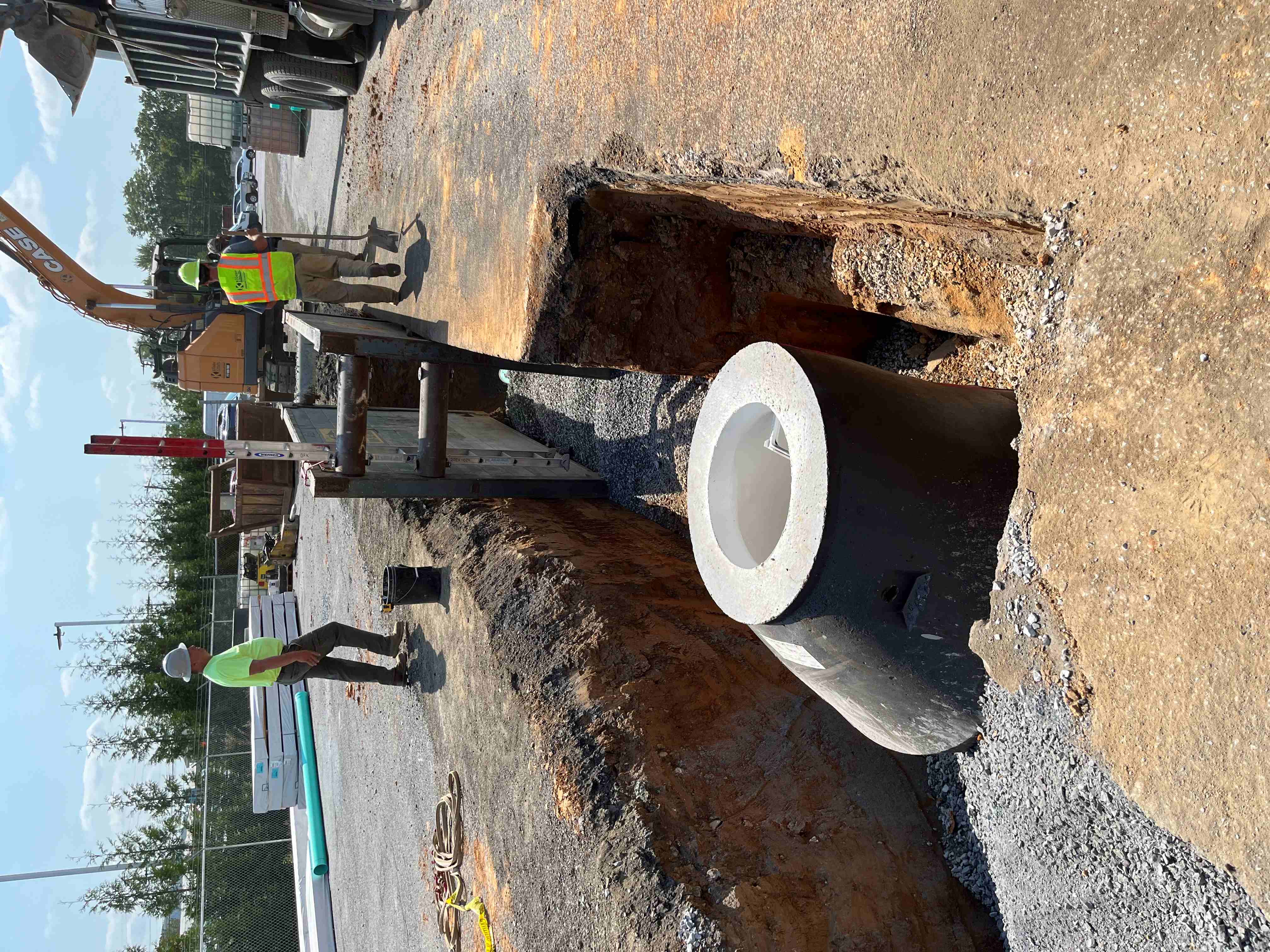 Crew setting a large concrete storm utility pipe in an open trench